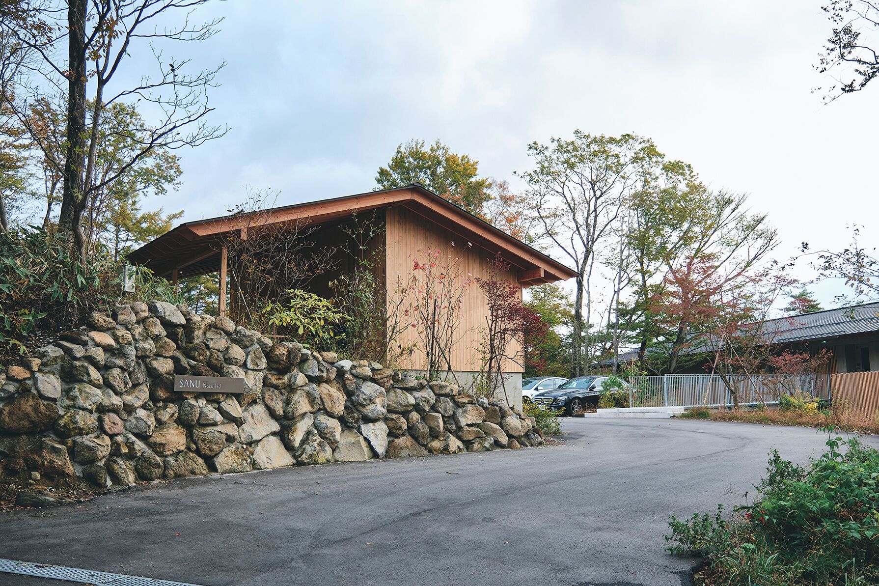 A stone wall with a wooden structure, a paved road, and parked cars.