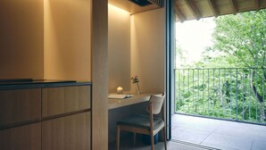 Une chambre moderne avec un bureau et une chaise, une petite table avec une bougie, et une vue sur la verdure depuis un balcon.