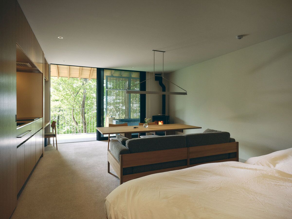 Un dormitorio moderno con una cama grande, un banco de madera y una zona de comedor con mesa y sillas.