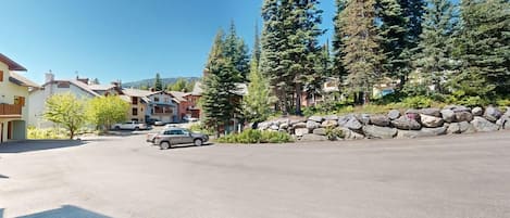 A residential street with houses, parked cars, and a stone wall.