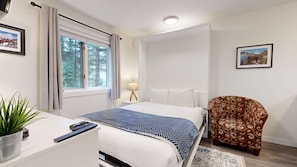 Ein Hotelzimmer mit Bett, Schreibtisch mit Pflanze, Stuhl, Lampe und einem Fenster mit Vorhängen.