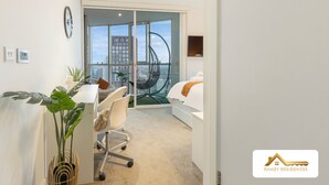 A modern bedroom with a bed, a desk, and a chair. There is a large window with a view of buildings and a hanging chair. - 2BR 2Bath Central London Luxury Flat Skyview (London)