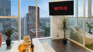 A modern living room with a large window, a flat-screen TV displaying 'NETFLIX', and a view of the cityscape. - 2BR 2Bath Central London Luxury Flat Skyview (London)