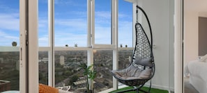 Une chambre moderne avec une grande fenêtre, un fauteuil suspendu et une vue sur la ville.