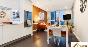 A modern kitchen with a dining area, featuring a large window, a clock, and a flat-screen TV. - 2BR 2Bath Central London Luxury Flat Skyview (London)