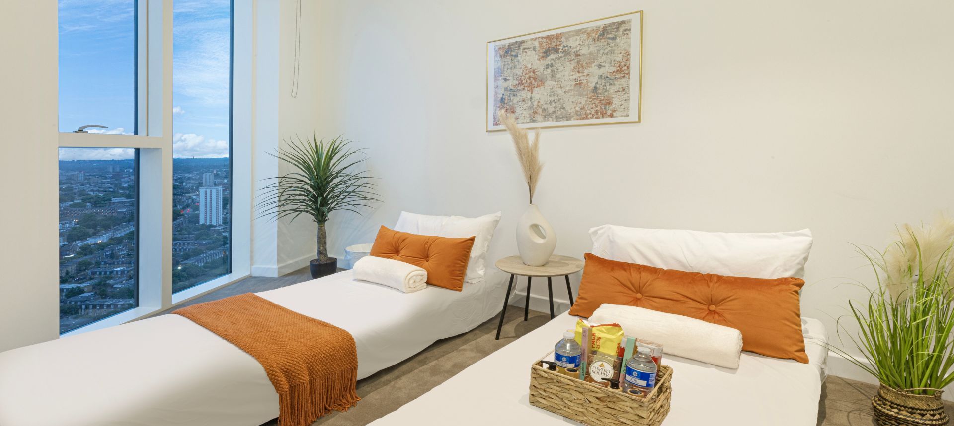 Ein Hotelzimmer mit zwei Betten, Blick auf die Stadt, einem Gemälde und einem Tablett mit Pflegeprodukten.