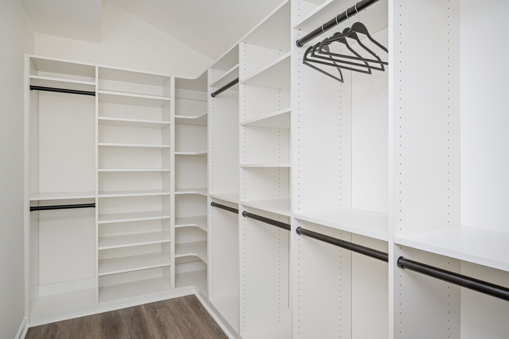 A walk-in closet with open shelving, hanging rods, and a metal rod for storage.