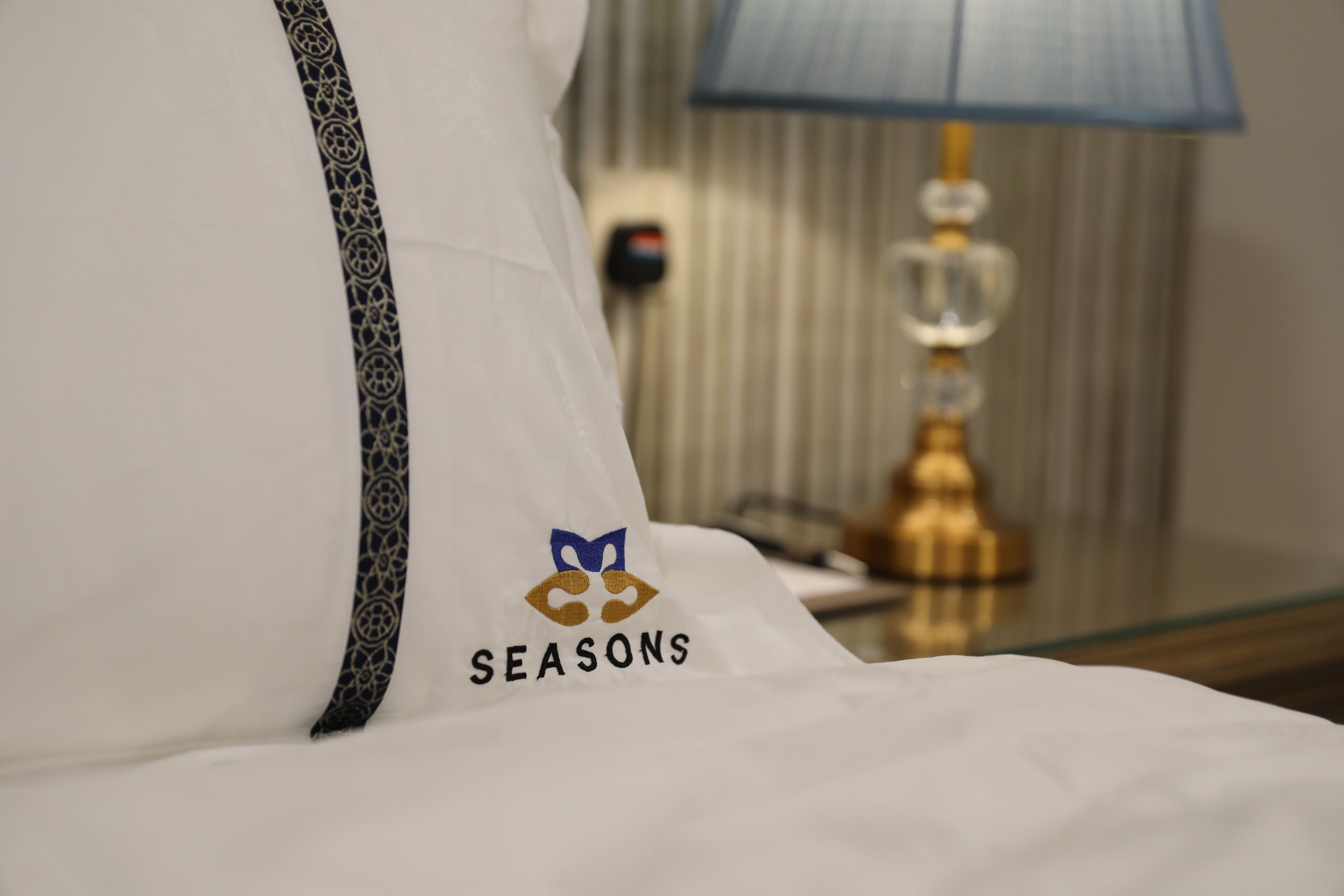 A hotel pillow with a logo and the word 'SEASONS' embroidered on it.