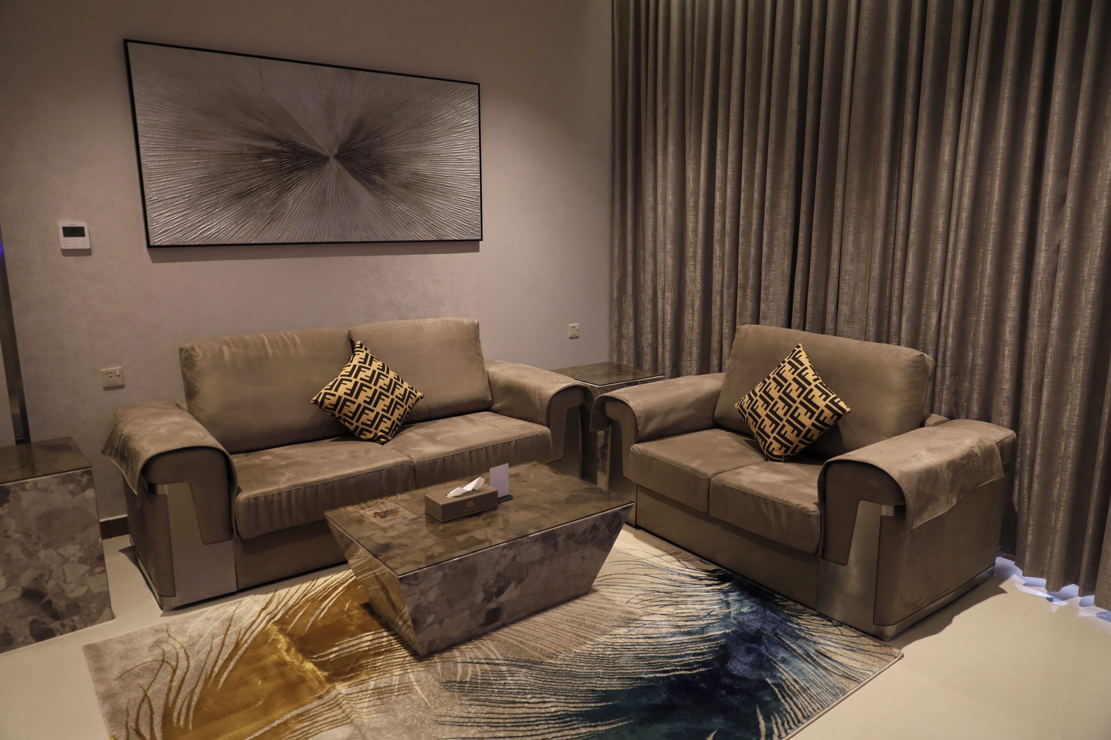A modern living room with two sofas, a coffee table, and a large abstract painting on the wall.