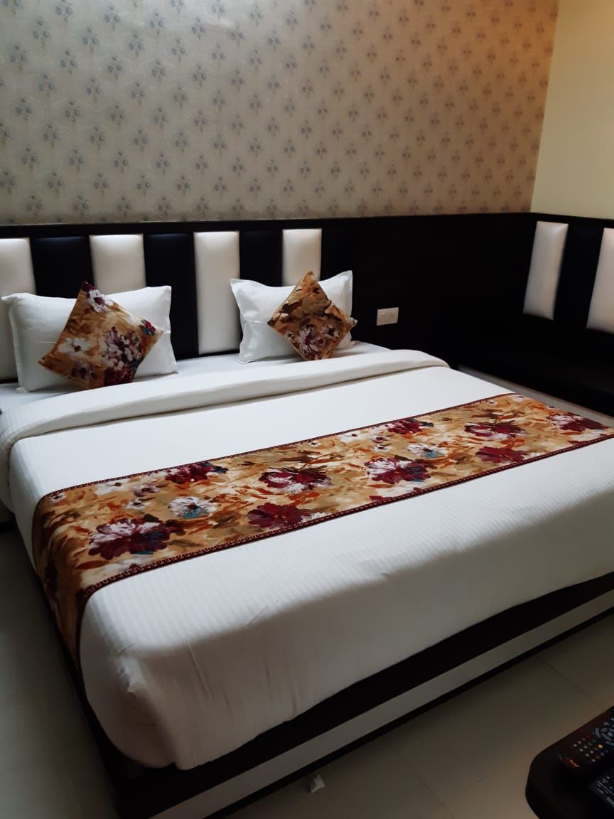 Una cama bien hecha con una colcha estampada con flores, dos almohadas y un control remoto al lado.