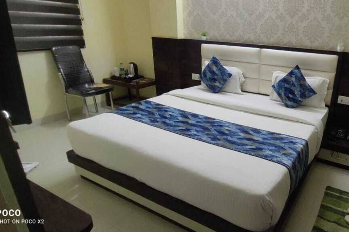 Un lit bien fait, recouvert d’une couvre-lit à motifs, une table de chevet avec une lampe et une chaise dans une chambre d’hôtel.