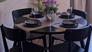 Ein Essbereich mit einem runden Tisch, schwarzen Stühlen, einer Deckenleuchte, einem Spiegel und einer Vase mit violetten Blumen.