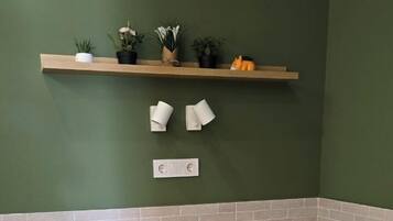 Une chambre à coucher avec un lit, des oreillers, une étagère avec des plantes et une prise électrique au mur.