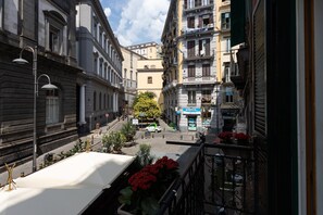A narrow street with buildings on both sides, a parked car, and a shop with a blue sign. - Palazzo il Convento Università (Naples)