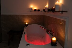 Une salle de bain avec une baignoire, une étagère avec des bougies et un miroir.