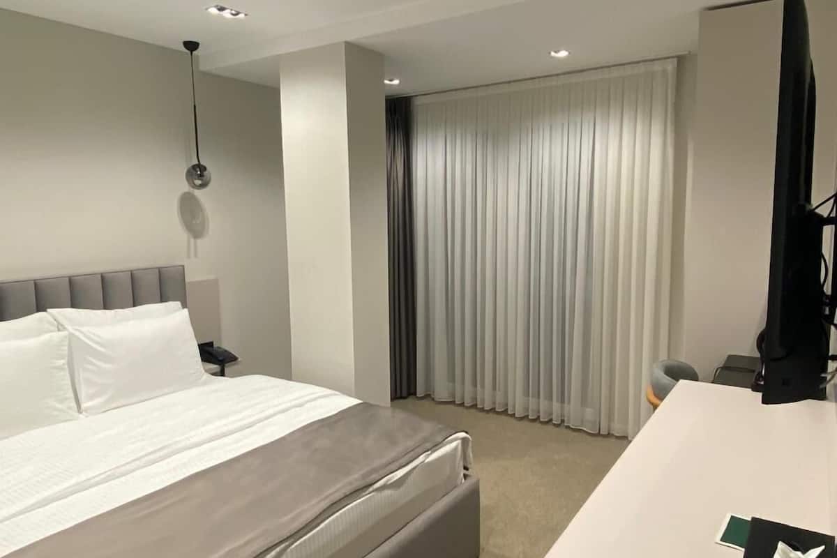 A hotel room with a bed, a desk, a chair, a TV, and a window with curtains.