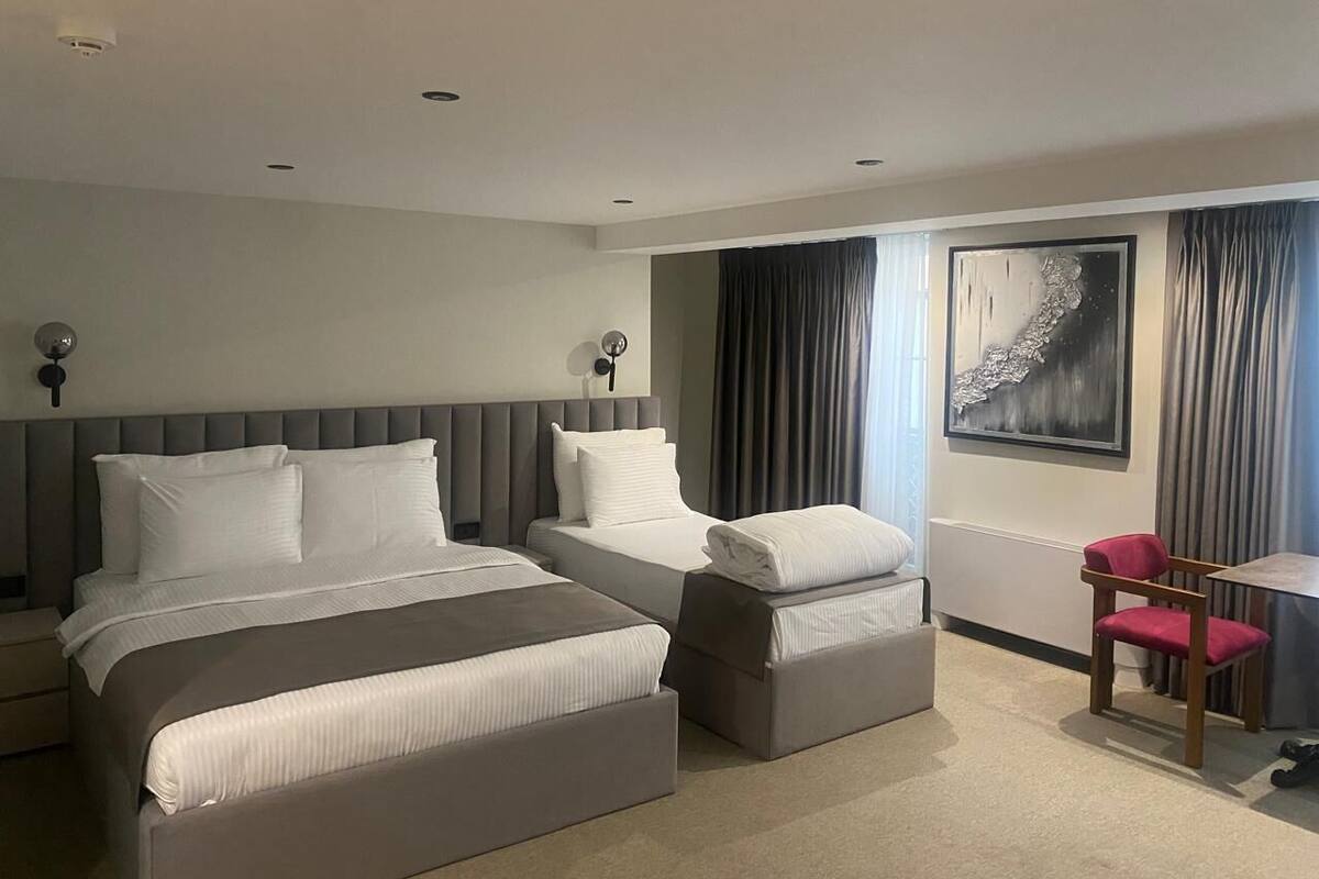 A hotel room with two beds, a desk, a chair, and a large window with curtains.