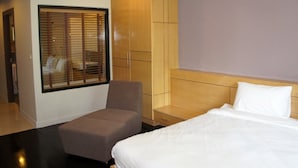 Une chambre d’hôtel avec un lit, une chaise, une armoire et une fenêtre avec des stores.