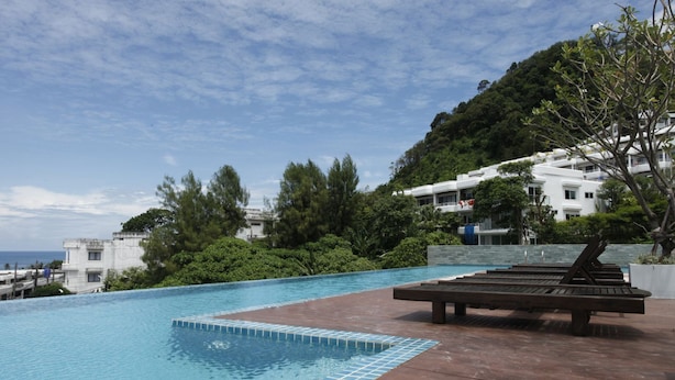 Une piscine dotée d’une terrasse en bois et de chaises longues, entourée d’une végétation luxuriante et offrant une vue sur une colline.
