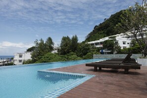 Una piscina con un pontile in legno e lettini, immersa nel verde e con vista su una collina.
