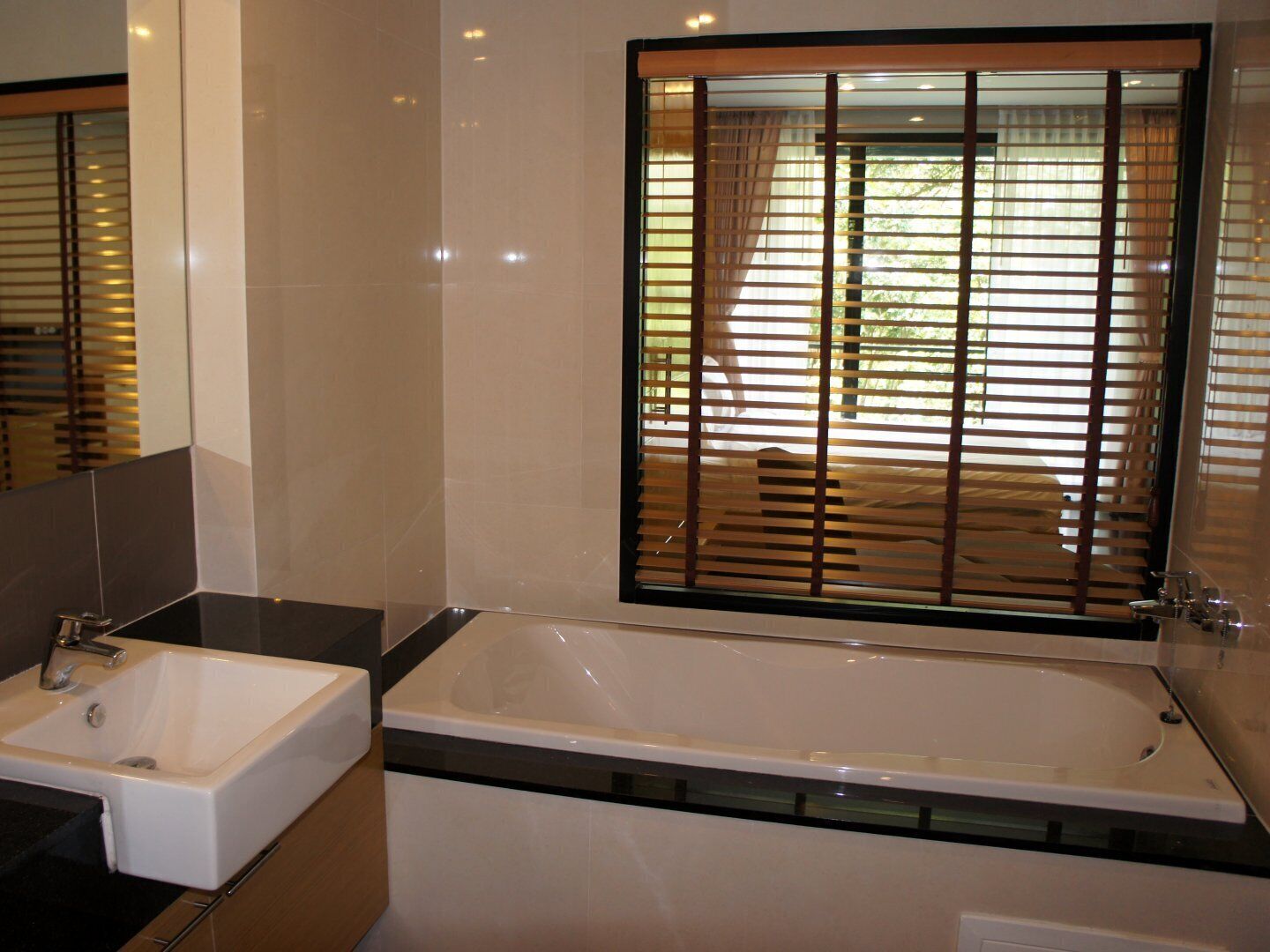 Ein modernes Badezimmer mit einer großen Badewanne, einem Waschbecken und einem Fenster mit Jalousien.