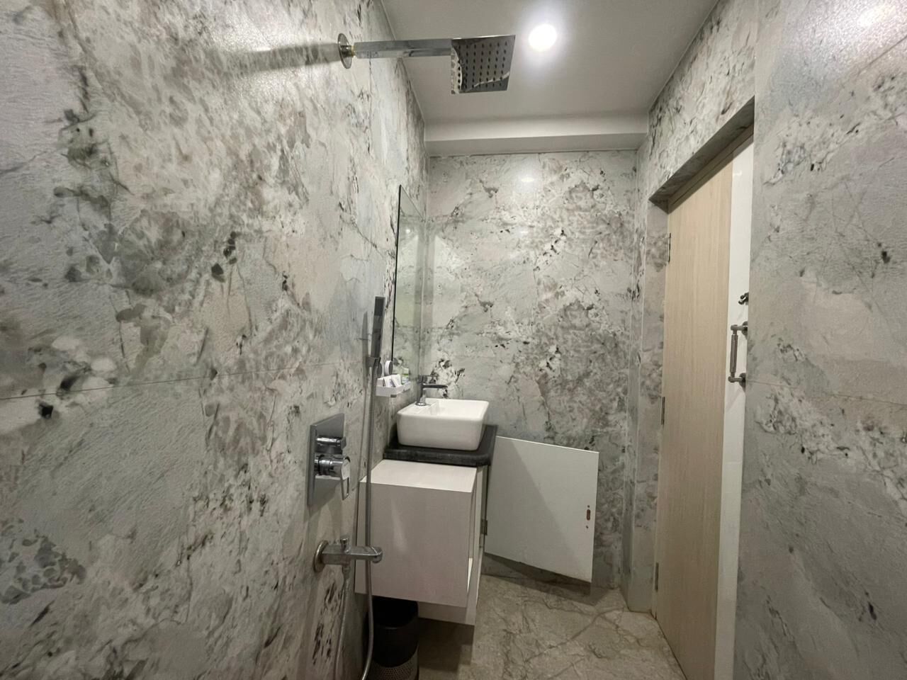 Un baño con pared de mármol, un lavamanos, un espejo y una ducha.