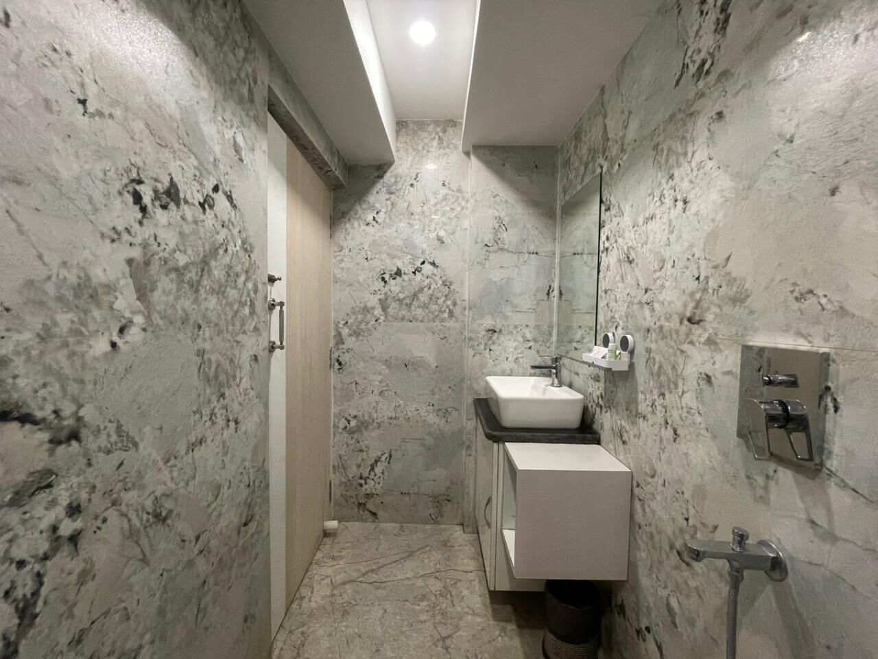 Une salle de bain avec un mur en marbre, un lavabo, un miroir et une douche.