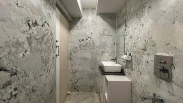 Une salle de bain avec un mur en marbre, un lavabo, un miroir et une douche.