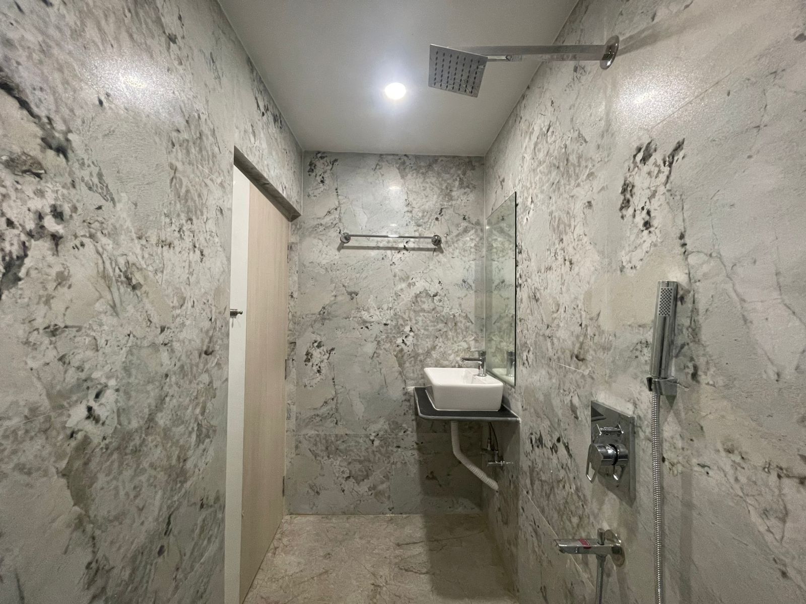 Un baño con pared de mármol, un lavamanos, un espejo y una ducha.
