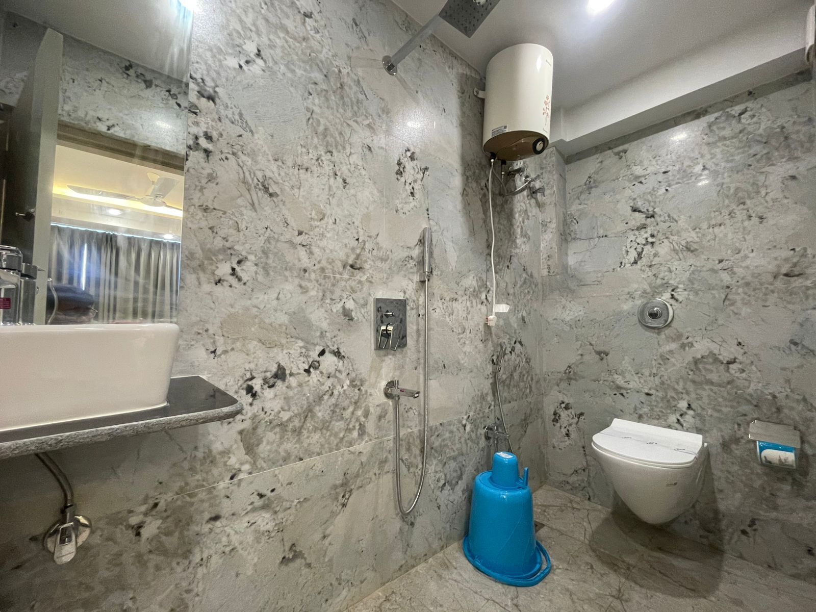 A bathroom with a marble wall, a white sink, a toilet, and a shower area.