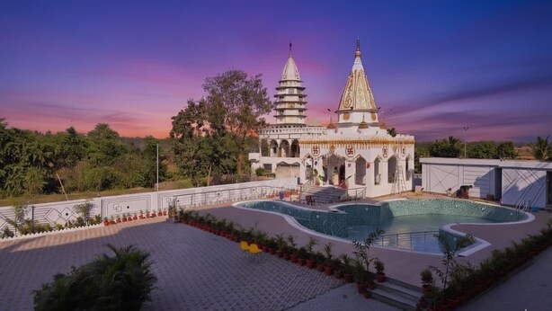 A temple with a large central tower and a smaller adjacent structure, surrounded by a landscaped area with a pool.