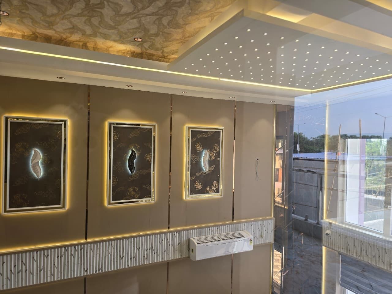 A modern interior with three framed artworks on the wall, a built-in air conditioning unit, and a view of the outside through a glass door.
