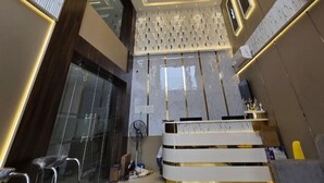 A modern hotel lobby with a central seating area, a reception desk, and a patterned wall.