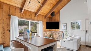 A modern living room with a wooden ceiling, a stone accent wall, a flat-screen TV, a white sofa, and a dining area with a wooden table and chairs. - Tramway Treat | Ski Heavenly | Mountain Views (Stateline)