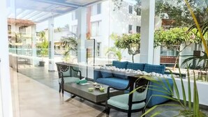 A spacious indoor area with a sofa and a table, surrounded by large windows and potted plants. - The Coastal Nest - 2BHK by Da Alohas (Nerul)