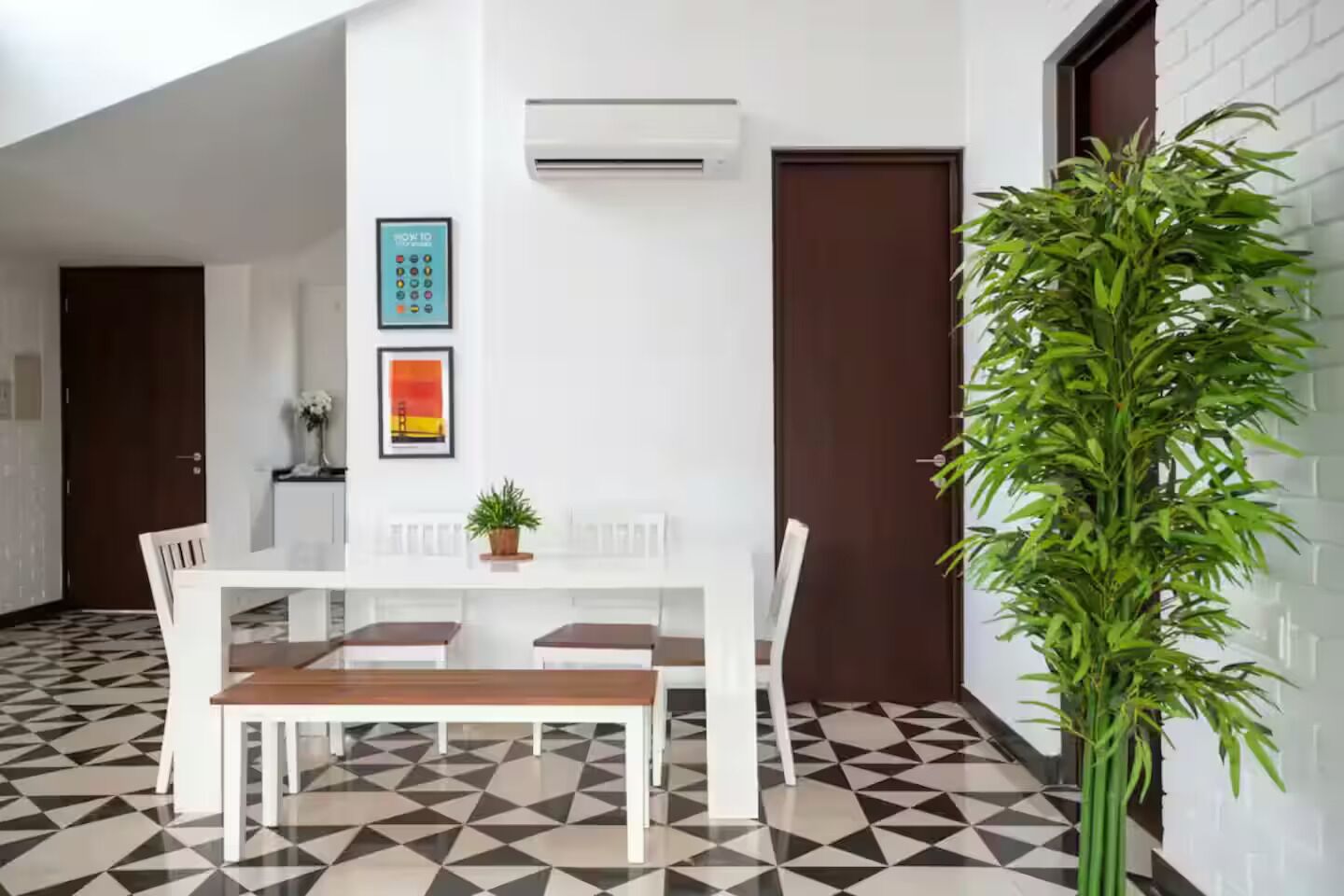 A dining area with a white table and chairs, a potted plant, and a wall-mounted air conditioner.