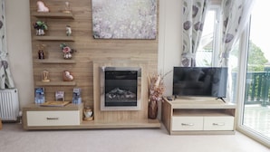 A living room with a fireplace, TV, wooden shelves, and a large window with curtains.