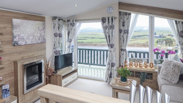 A modern living room with a TV, wooden furniture, a balcony with a view, and a sign that reads "CROESO".