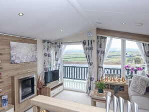 A modern living room with a TV, wooden furniture, a balcony with a view, and a sign that reads "CROESO". - Bryncrin (Pwllheli)
