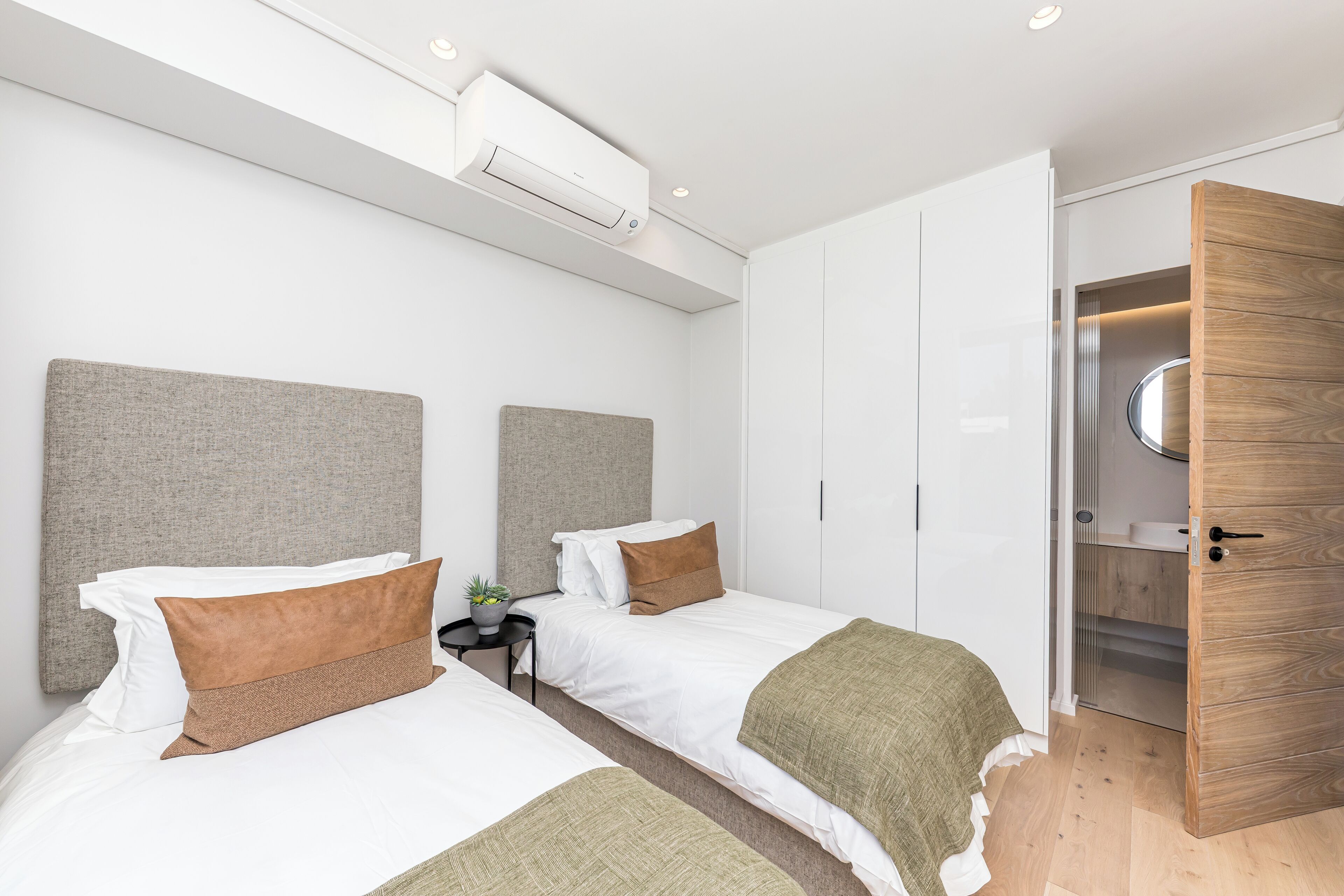Ein modernes Hotelzimmer mit zwei Betten, einem Kleiderschrank und einem eingebauten Spiegel.