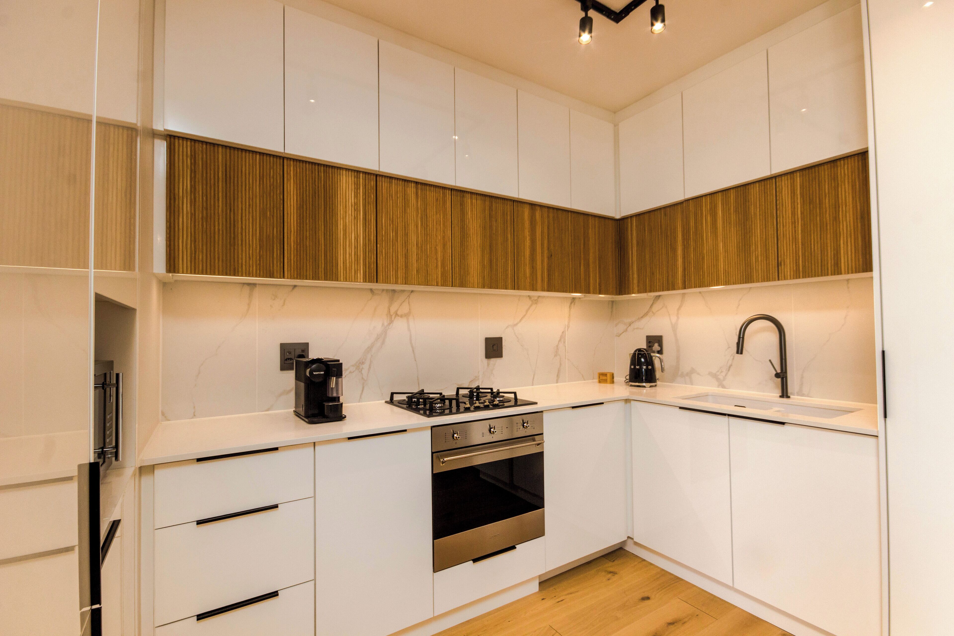 A modern kitchen with white cabinets, a wooden accent wall, a built-in oven, and a sink.
