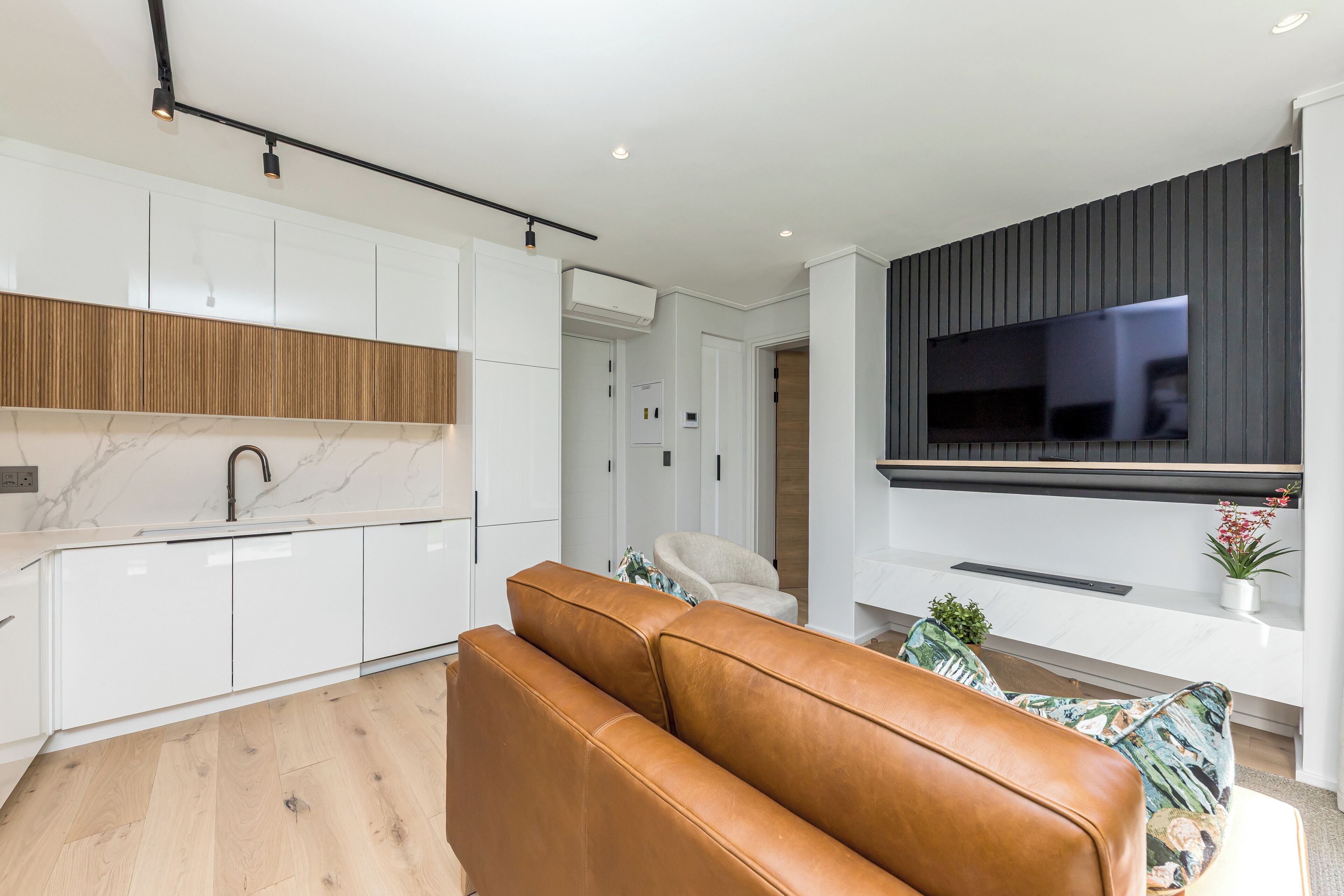 A modern kitchen with white cabinets, a marble countertop, and a leather sofa in the living area.