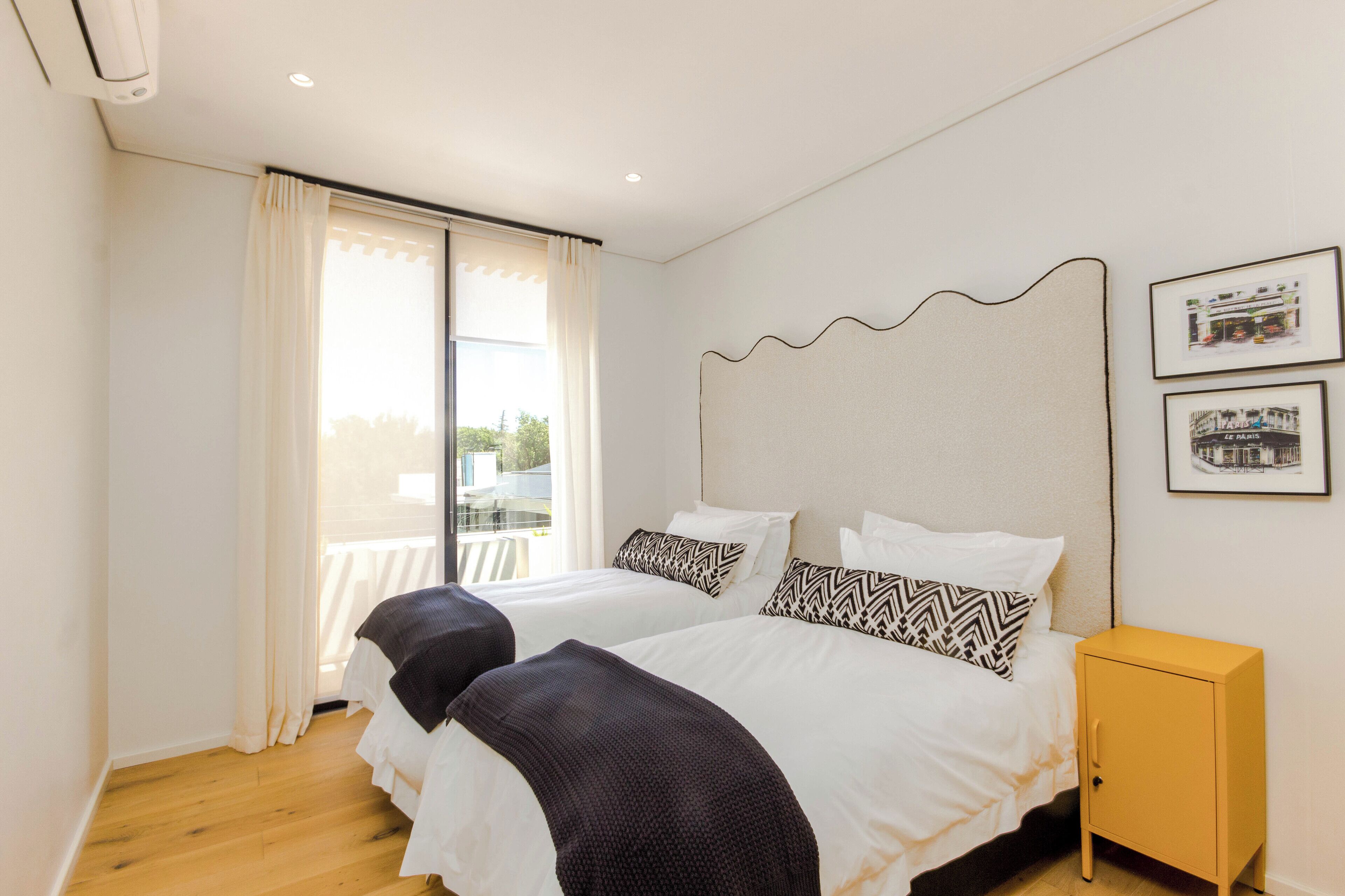 A hotel room with two beds, a small yellow cabinet, and a balcony with a railing.