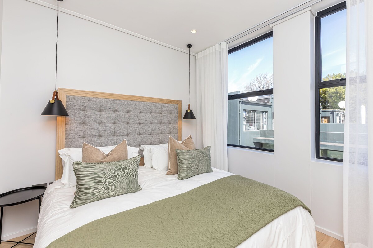 A modern bedroom with a large bed, a wooden headboard, and two pendant lights.
