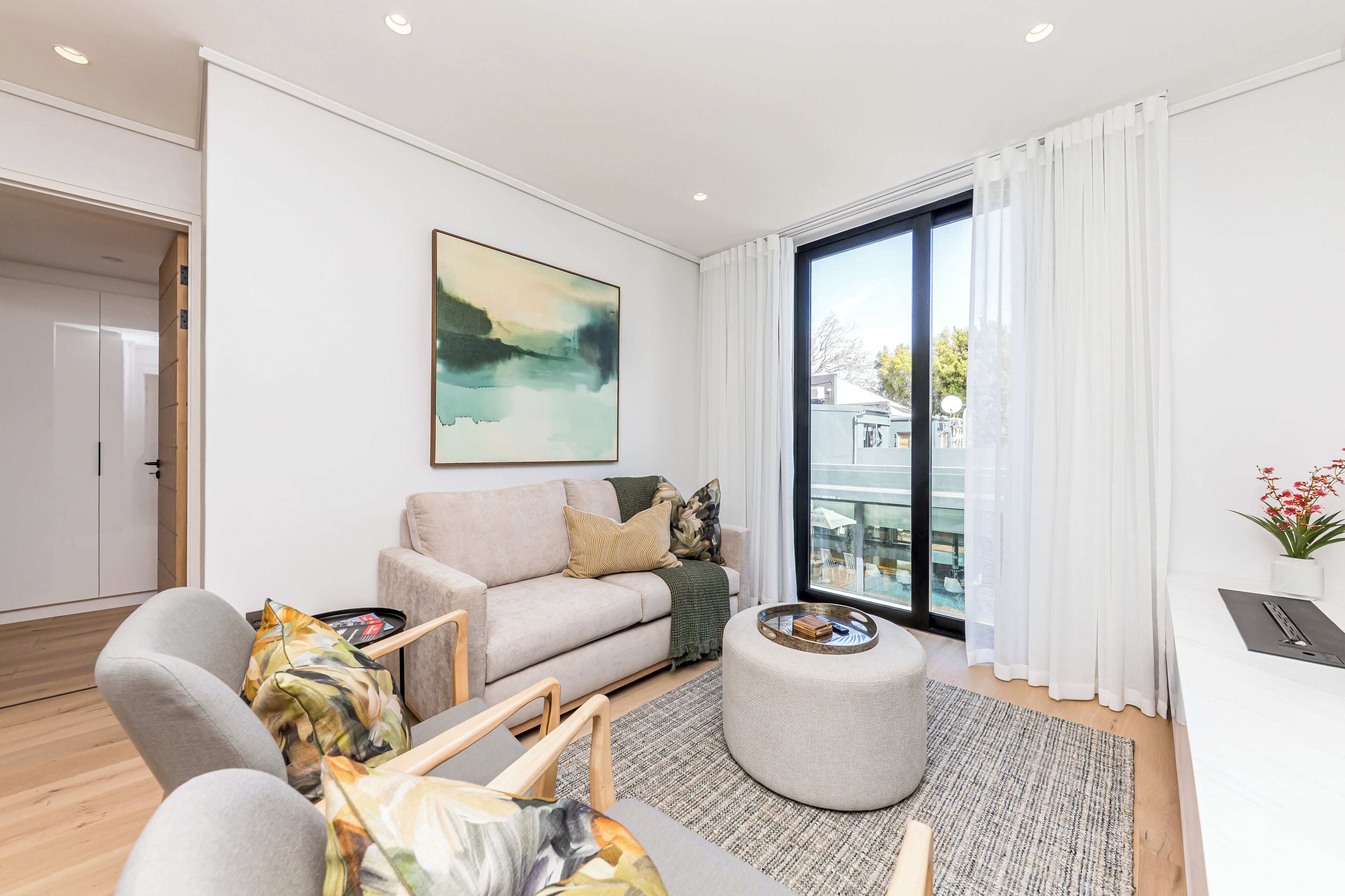 A modern living room with a sofa, chairs, a coffee table, and a large window with curtains.