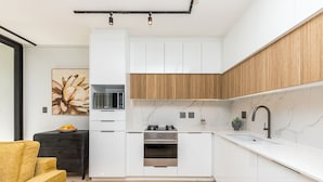 Une cuisine moderne avec des armoires blanches, un mur d’accent en bois, un plan de travail noir et un robinet noir.