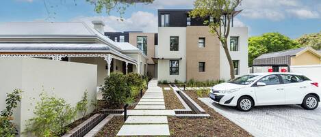 Rua residencial com casas modernas, um caminho de entrada pavimentado e um carro branco estacionado à direita.