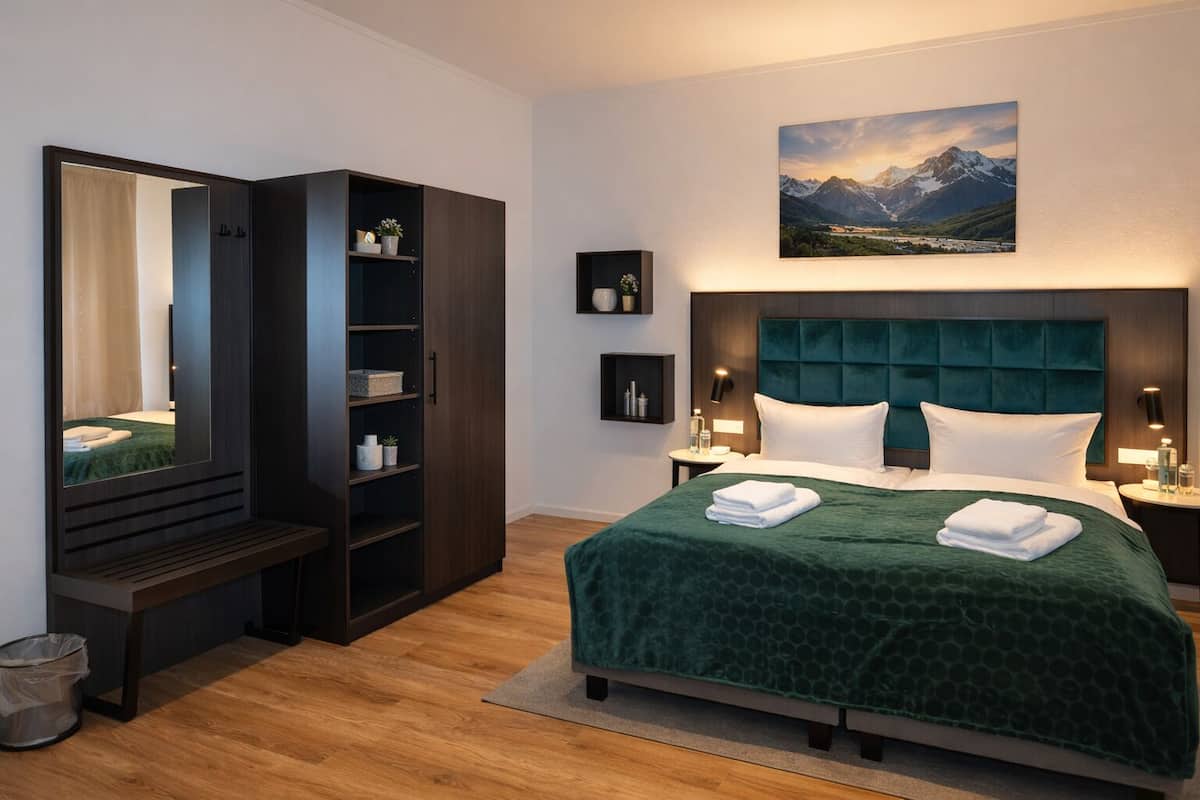 Een hotelkamer met een groot bed, een garderobe, een spiegel, een nachtkastje en een schilderij van bergen.