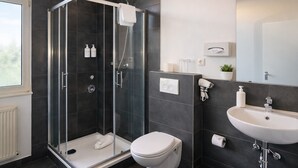 Une salle de bain moderne avec une douche à parois de verre, des toilettes blanches, un lavabo et un miroir.