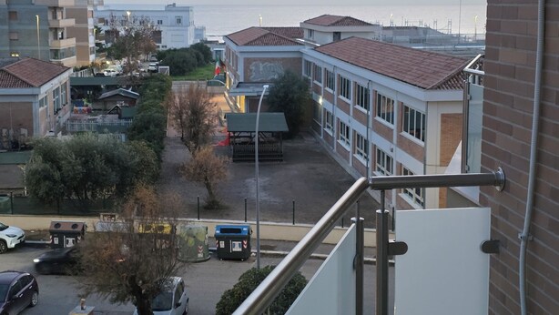A residential area with a view of the sea, featuring multi-story buildings, a parking area, and a small park with trees. - Stephen's Tourist Accommodation (Lido di Ostia)